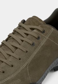 Olivengrønn semsket lærsko med flate lisser, svarte snøringer, synlige sømmer og en teksturert gummisåle. Har en lav profil design.