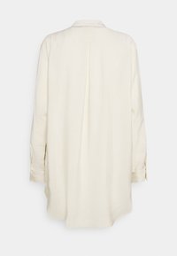 Langærmet cremefarvet skjorte med afslappet pasform, der har krave, knapmanchetter og en vertikal søm på ryggen som designdetalje.