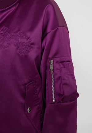 Paarse satijnen bomberjack met geborduurd logo, één met rits sluitend mouwvak en een patch pocket, met een soepele textuur en een ontspannen pasvorm.