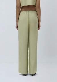 Pantaloni verde chiaro a gamba larga realizzati in un tessuto liscio con una vestibilità rilassata, dotati di una vita arricciata e senza tasche visibili.
