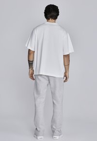 Balta pārāk liela T-kreklu ar īsām piedurknēm, pārī ar gaiši pelēkiem treniņbikšu. Gluda tekstūra un vienkāršs dizains, nav redzamu rakstu.