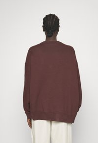 Oversized vinröd sweatshirt tillverkad av mjukt tyg. Har rund halsringning, sänkta axlar samt ribbstickade muddar och fåll. Enkelt, enfärgat mönster.