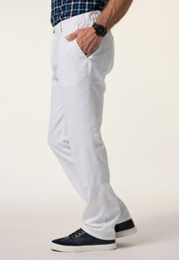 Vita, lätta byxor med elastisk midja, sidofickor och rak bendesign, bärs med marinblå sneakers mot en ljus bakgrund.