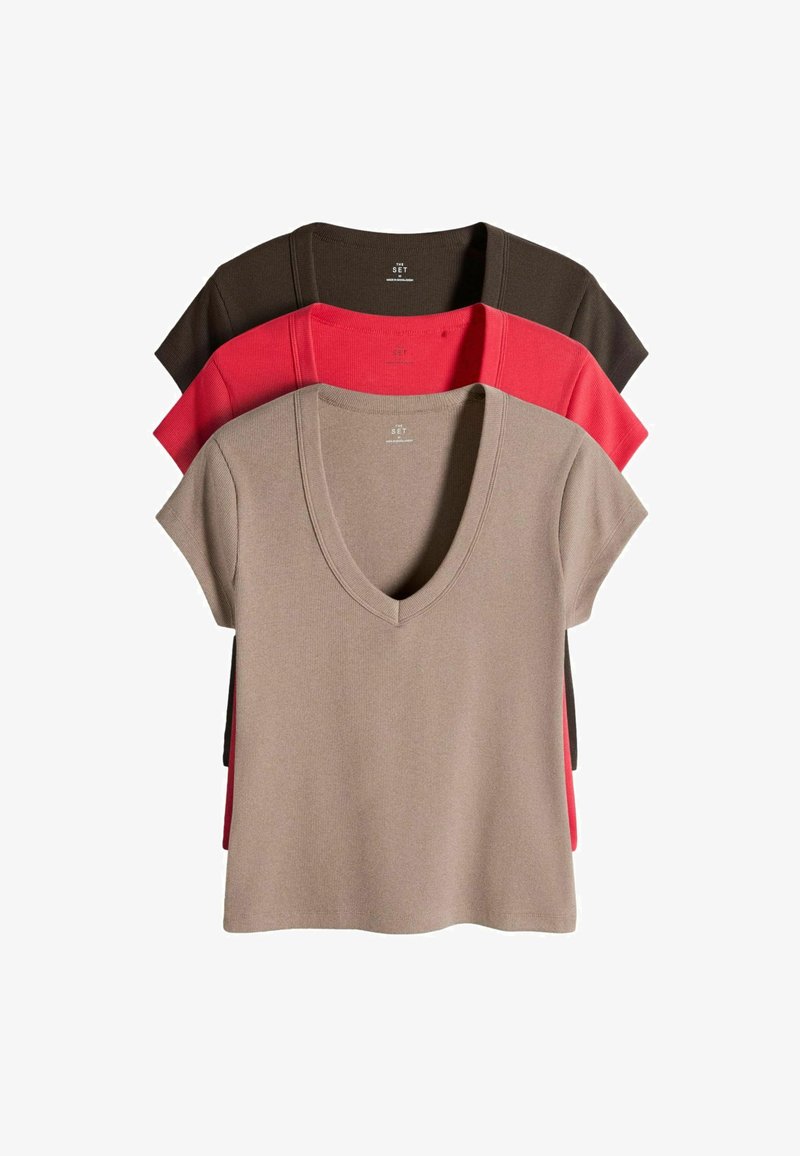 Trois hauts en maille à manches courtes avec col en V empilés, en beige, rouge et marron foncé, affichés sur un fond blanc.
