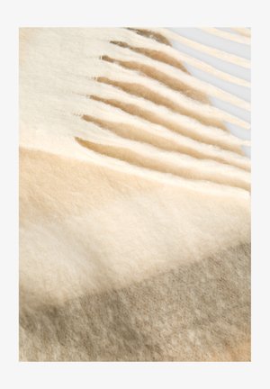 Wełniany koc w gradientach kremowego, beżowego i taupe, z miękką teksturą i frędzlami na krawędziach dla dodatkowego akcentu.