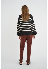 Suéter a rayas en blanco y negro con ajuste oversize, combinado con pantalones de color óxido. Textura suave y silueta relajada.
