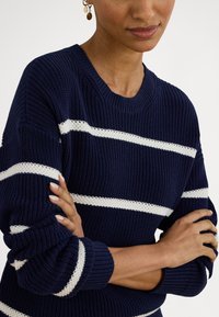 Námornícky modrý pletený sveter s bielymi vodorovnými pruhmi, rebrovaným okrúhlym výstrihom a manžetami, s textúrovaným vzorom a pohodlným strihom.