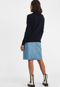Marineblaue strukturierte Sweater, Jeansrock und beigefarbene Ankle Boots mit schwarzen Akzenten. Fokus auf lässiger, geschichteter Outfit-Silhouette.
