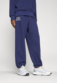 Navy kék, puha anyagból készült melegítőnadrág, elasztikus derékkal és bokakötéssel, fehér hímzéssel ellátott "Under Armour" logóval.