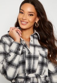 Schwarz-weißer Karomuster Shacket aus weichem Stoff, mit Knopfleiste, zwei Brusttaschen und einem Gürtel. Strukturierter Musterverlauf.