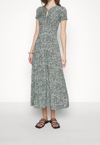Maxi dress with short sleeves, black and green textured pattern, v-neckline with keyhole detail, flowing fabric, paired with black strappy sandals.
