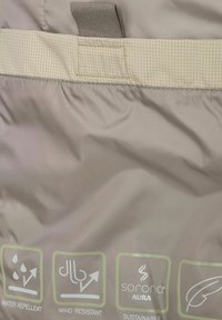 Wasserabweisender beiger Stoff mit einem strukturierten, braunen Bund. Enthält Symbole für wasserdicht, windresistent und Informationen zur Nachhaltigkeit.