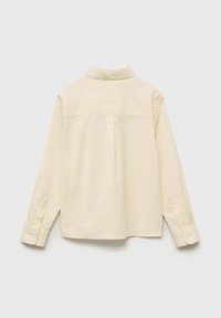 Majica s dolgimi rokavi v kremni barvi, z značilnim ovratnikom, detajlom na hrbtni strani in manšetami na gumb, izdelana iz mehkega materiala.