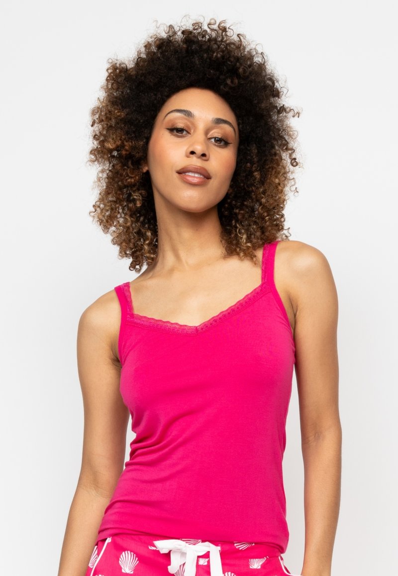 Camiseta sin mangas ajustada de color rosa con tirantes delgados, escote en V y borde de encaje. Tejido suave y textura lisa. Combinada con pantalones cortos con estampado.