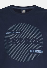 Marineblå bomulds t-shirt med et cirkulært grafik med diagonale striber. Teksten lyder "WRECKING CREW," "PETROL," og "ALASKA" i kontrastfarver.