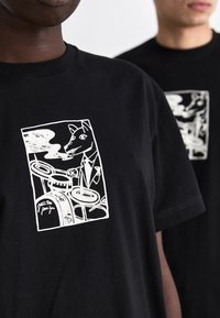 Črno bombažno majico z belim grafičnim printom psa v smokingu, ki igra na bobne, z dimom in glasbenimi elementi. Standardna prileganje.