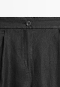 Czarne spodnie z pojedynczym zapięciem na guzik, plisowanym przodem i bocznymi kieszeniami. Materiał ma teksturowany, tkany wygląd.