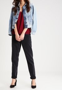 Jeansjacka med ljus tvätt, korta ärmar och knappstängning, tillsammans med en vinröd topp och svarta byxor med uppvikt fåll. Svarta klackar fulländar outfiten.