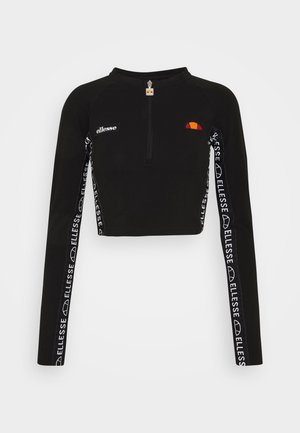 Svart kort topp med långa ärmar, halvlång dragkedja vid kragen och vit märkesband längs ärmarna. Har en färgstark logotyp på bröstet.