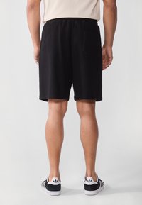 Schwarze Shorts aus strukturiertem Material, mit einem elastischen Bund und einer Gesäßtasche. Getragen mit schwarz-weißen Sneakers.