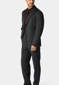 Dunkelgraues Anzug mit einreihiger Jacke und passender Hose, kombiniert mit einem braunen Hemd. Glatte Textur, taillierte Passform und minimale Details.