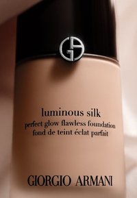 Fond de teint Luminous Silk de Giorgio Armani dans un flacon beige avec un couvercle noir et un logo argenté, affichant les détails du produit en texte noir.