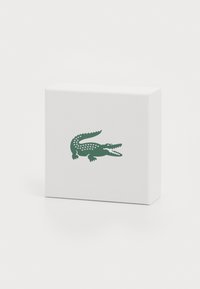 Scatola bianca con una superficie texture e un design del logo di coccodrillo verde, caratterizzata da motivi triangolari lungo la parte posteriore.