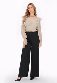 Beige Oberteil mit Rüschensleeven und strukturiertem Oberteil, kombiniert mit schwarzen weit geschnittenen Hosen und schwarzen Absätzen. Schlichtes, elegantes Design.