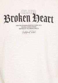 Weißes Baumwoll-T-Shirt mit fettem schwarzen Text: "CLUB Broken Heart" und kleinerem Text darunter. Legeres Design mit standardmäßiger Passform.
