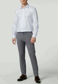 Vit långärmad skjorta med knappar, kombinerad med grå mönstrade slim-fit-byxor, bärs med mörkbruna skor. Slät tyg, skräddarsydd design.