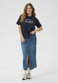 T-shirt navy avec le texte "MIDNIGHT IN PARIS", associé à une jupe en denim taille haute et longueur cheville avec une fente à l'avant. Des baskets blanches complètent le look.