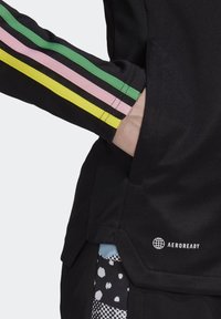Black athletic jacket with multicolored striped accents in green, pink, and yellow on sleeves; features a side pocket and "AEROREADY" logo.