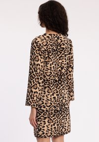 Robe à motifs léopard en beige et noir, dotée d'une coupe décontractée et de manches longues, fabriquée dans un tissu lisse au toucher doux.