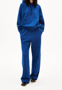 Niebieska bluza z kapturem z przednią kieszenią, w komplecie z pasującymi niebieskimi dresami. Obydwa elementy wykonane z miękkiej, grubej tkaniny, charakteryzują się luźnym krojem.