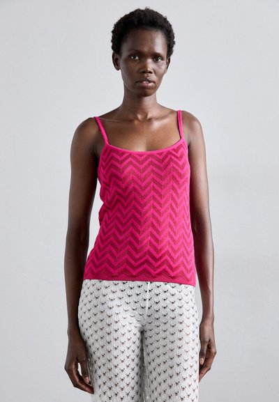 Top de tirantes finos con patrón de chevron en color rosa, combinado con pantalones blancos semi-transparentes con un patrón que incluye pequeños acentos oscuros.