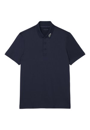 Polo de manga corta azul marino con tapeta de dos botones y pequeño logo de cocodrilo en verde, blanco y rojo en el cuello.