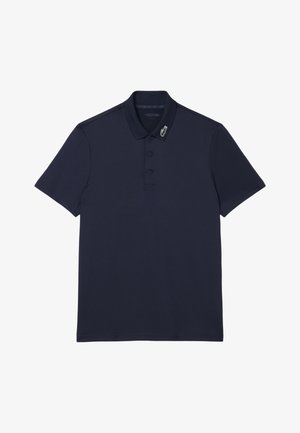 Polo bleu marine à manches courtes avec patte de boutonnage à deux boutons et petit logo crocodile vert, blanc et rouge sur le col.