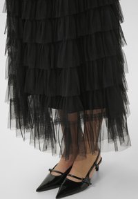 Black tiered tulle skirt with layered frills. Pointed black heels with a slingback strap and decorative hardware detail. Transparent texture.