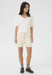 Krämfärgad t-shirt med kort ärm och v-ringning, kombinerad med beiga shorts med dragsko och mörkbruna snörskor. Mönstrade grå strumpor.