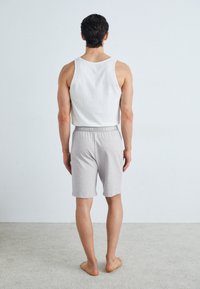 Biały bawełniany tank top i szare szorty dżersejowe z elastycznym pasem, z logo na pasku. Model stoi boso, zwrócony tyłem.