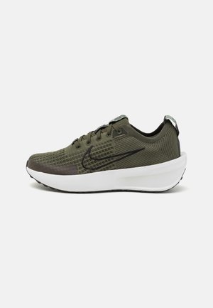 Baskets en tricot vert olive avec le logo Nike noir, lacets noirs et semelle blanche épaisse, présentées de profil extérieur sur fond blanc.