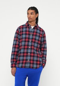 Rød, marineblå og hvid ternet skjorte med knaplukning, lange ærmer og klassisk krave. Påsat blå sweatpants.
