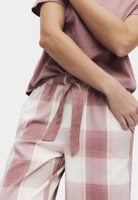 Ljusrosa t-shirt kombinerad med rutig byxa i rosa, creme och vitt. Byxorna har dragsko i midjan och ett mjukt tyg.