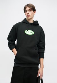 Hanorac negru cu buzunar tip cangur și glugă cu siret. Prezintă un logo grafic verde pe piept. Material moale, croială lejeră.