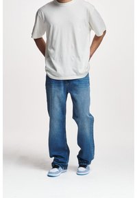 Vit bomulls-t-shirt, blå jeans i denim med en lätt blekning och blåaccenterade sneakers med en klassisk silhuett. Avslappnad outfit.