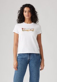Witte katoenen t-shirt met een kleurrafische afbeelding met de tekst "Levi's", korte mouwen en een relaxte pasvorm, gecombineerd met blauwe denim jeans.