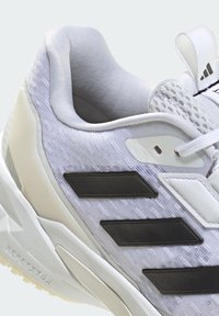 Buty sportowe Adidas z teksturowaną górną częścią w jasnoszarym kolorze, trzema czarnymi paskami, białymi akcentami i wzmocnioną gumową podeszwą.