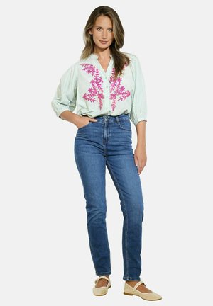Blusa de rayas verde claro con bordado floral rosa, combinada con jeans de mezclilla azul de cintura alta y zapatos planos beige.