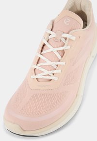 Scarpa da ginnastica rosa chiaro con tomaia in rete testurizzata, lacci bianchi e suola color crema. Presenta una punta liscia e dettagli con logo.