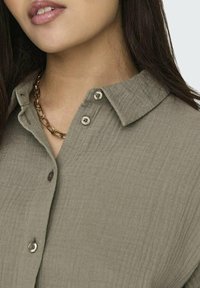 Groen gestructureerd overhemd met knopen en een kraag, voorzien van zilveren knopen en een gouden ketting.